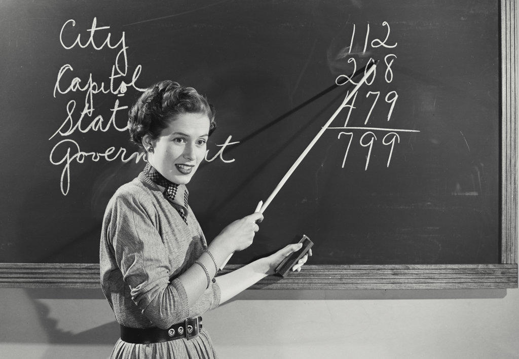 Teacher standing at chalkboard pointing to numbers