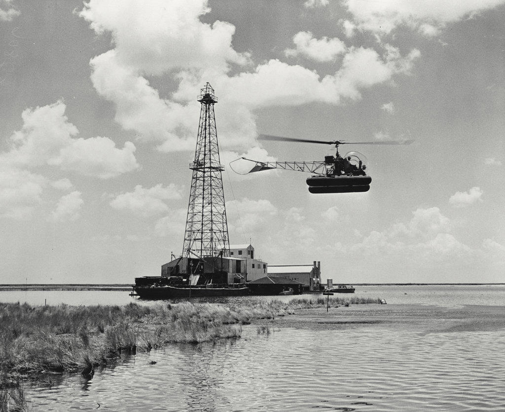 A Bell Aircraft Model 47D-1 helicopter comes in for a landing beside an oil well in the Louisiana marshes