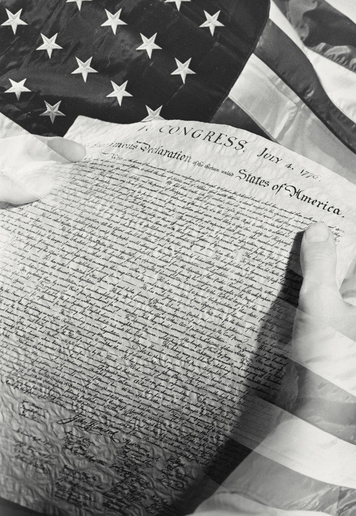 Photo illustration of hands holding Declaration of Independence in front of American flag