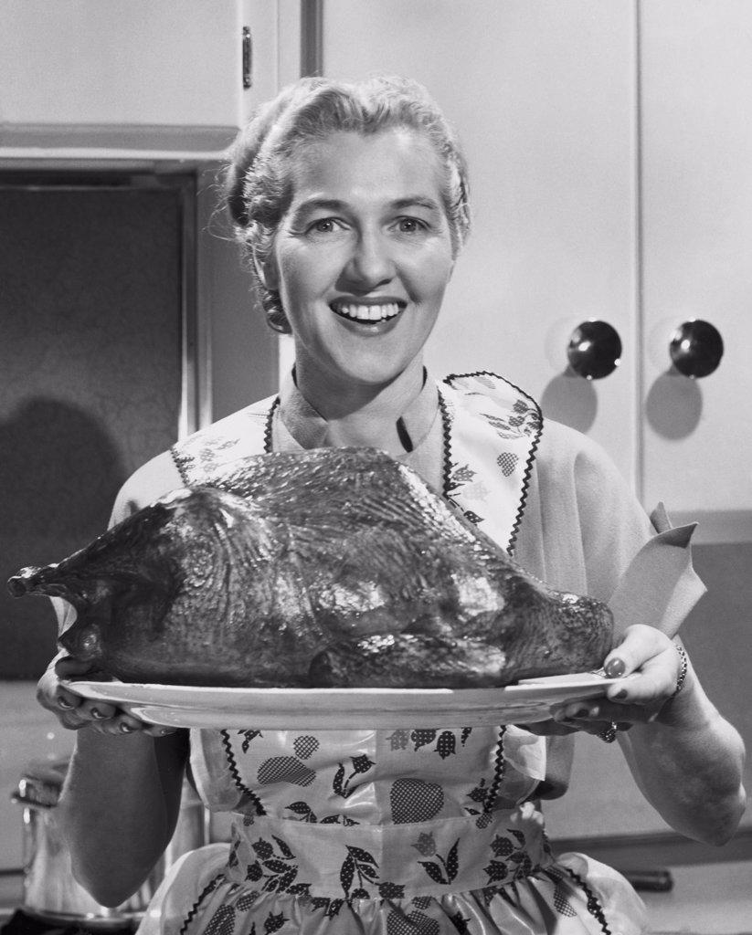 Mid adult woman holding a roast turkey and smiling