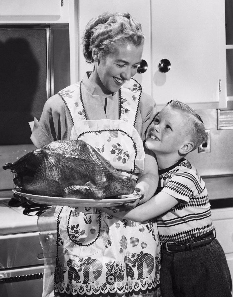 Mid adult woman holding a roast turkey with her son hugging her