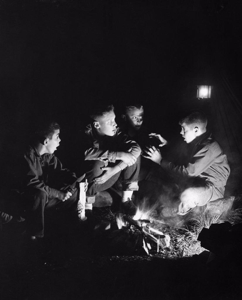 Boys listening to friend telling stories by campfire