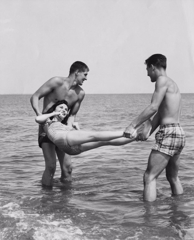 Two young men swinging a young woman over water