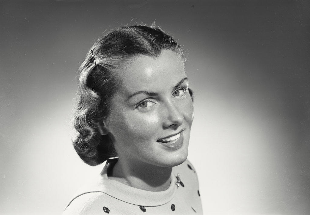 Woman with short hair in polka dot blouse smiling.