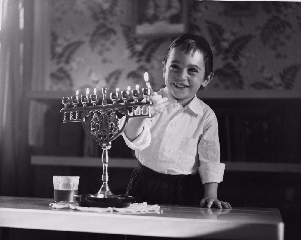 Boy lighting menorah candles and smiling