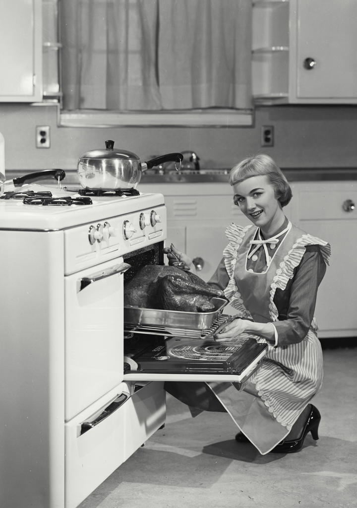 Portrait of a young woman putting a turkey into an oven