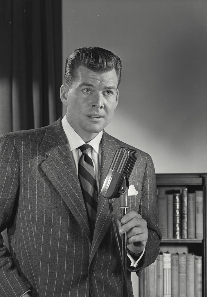 Man in pinstripe suit speaking into microphone looking away