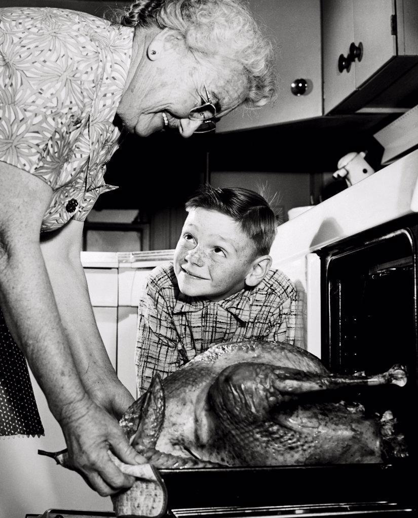 Grandmother taking a turkey from the oven with her grandson watching