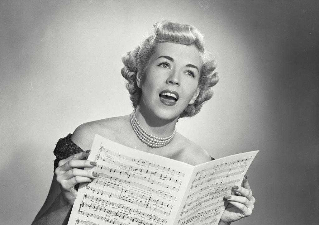 Portrait of woman in lace dress singing from sheet music