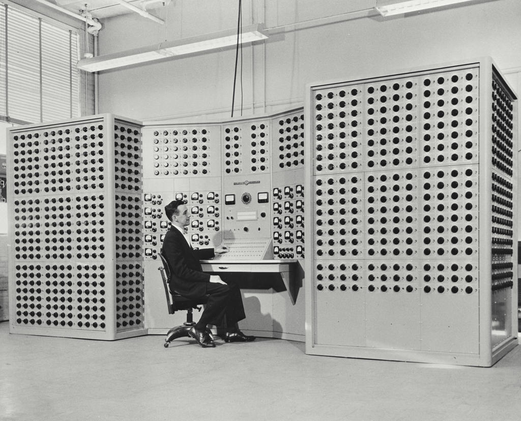 Man sitting in front of dial studded new computer that mathematically models a complex electric power system.