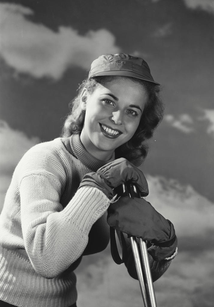 Woman in sweater and snow gloves leaning on ski poles.