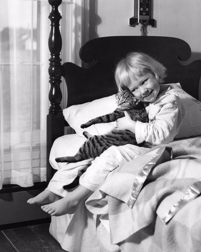 Girl sitting on bed and holding cat