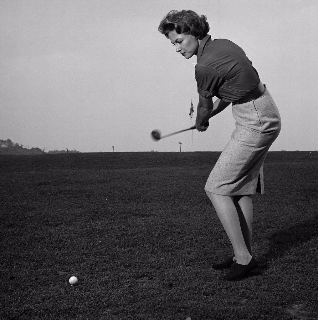 Mid adult woman swinging a golf club on a golf course