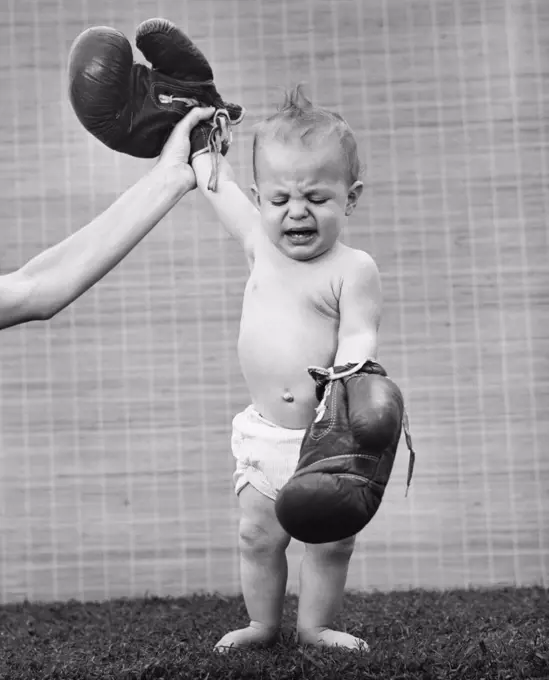 Person's hand raising a baby's hand wearing boxing gloves