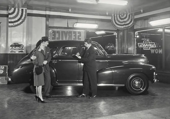 Couple in car dealership standing next to Chevrolet Stylemaster talking to salesman