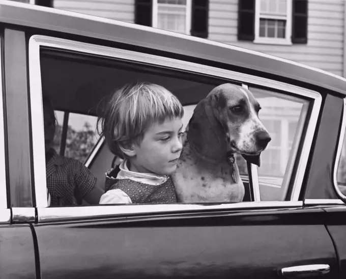Girl with her dog in car looking through window