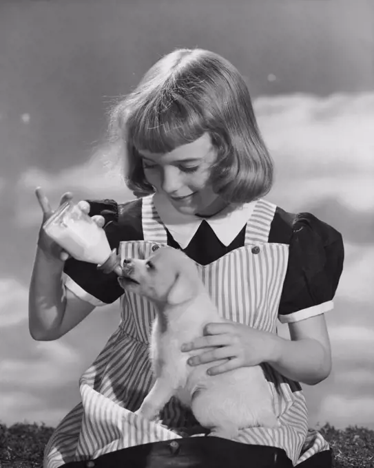 Girl feeding milk to a puppy from a baby bottle