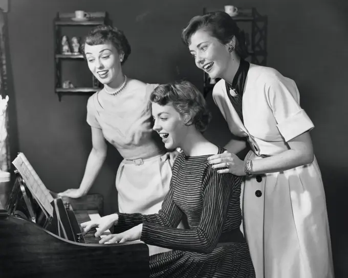Side profile of a young woman playing the piano with two young women standing behind her