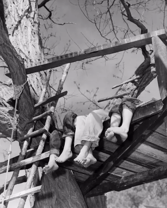 Low angle view of the legs and feet of three children in a tree house