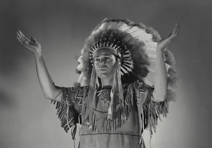 Native American man wearing traditional clothing and gesturing