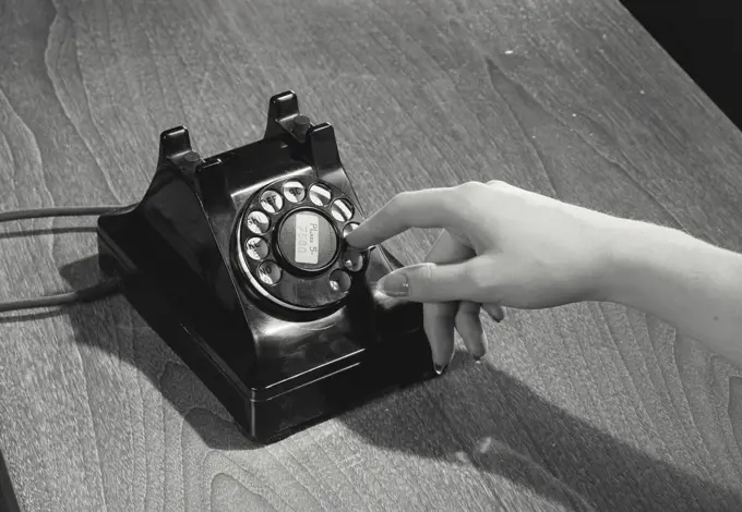 Vintage photograph. Close-up of a person's hand dialing a number on a rotary telephone