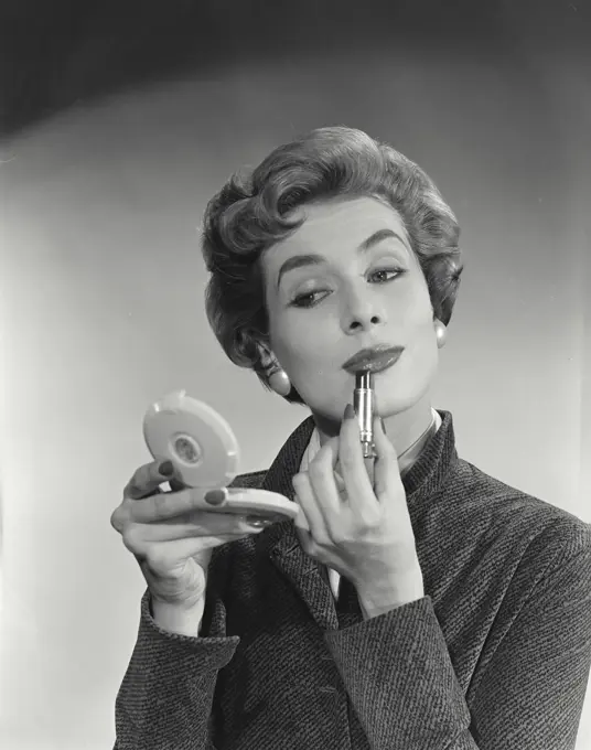 Vintage Photograph. Woman with short hairstyle putting on lipstick looking into compact mirror