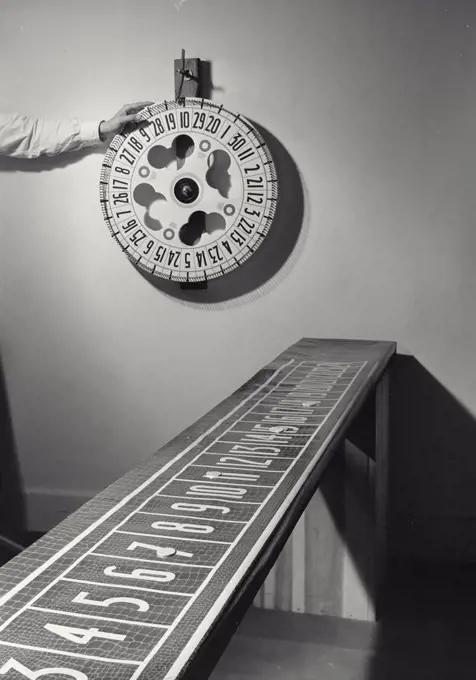 Vintage photograph. Hand about to spin Carnival Wheel on wall with betting board in foreground