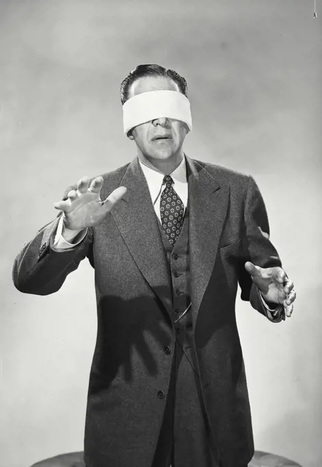 Vintage Photograph. Man in suit and tie wearing blindfold over eyes with hands reaching out in front