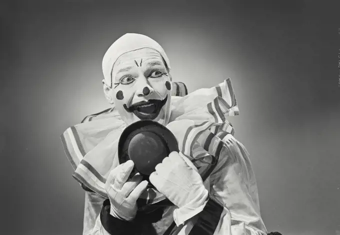 Vintage photograph. Portrait of clown holding silly hat with excited expression.