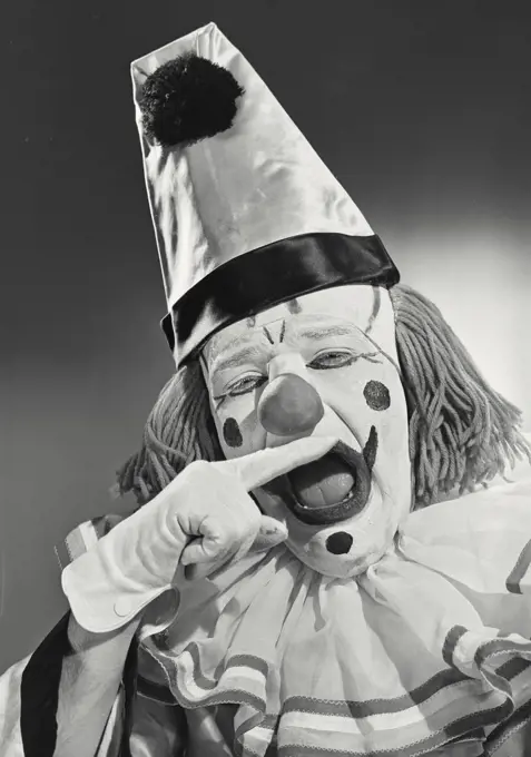 Vintage photograph. Portrait of clown wearing silly hat biting finger.