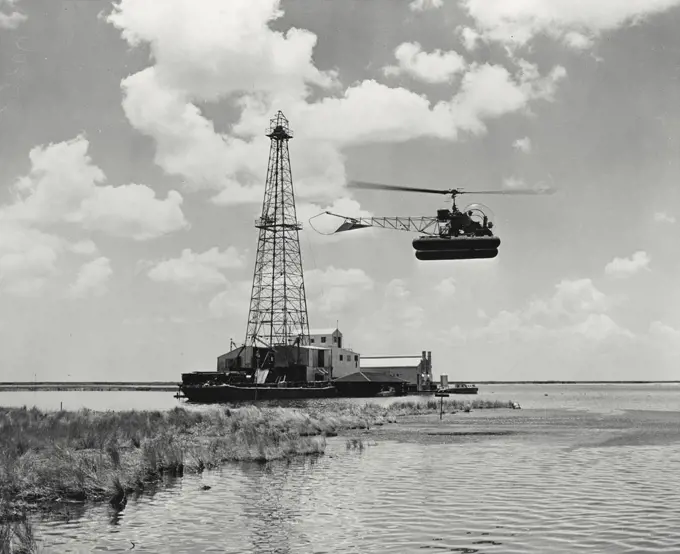 Vintage photograph. A Bell Aircraft Model 47D-1 helicopter comes in for a landing beside an oil well in the Louisiana marshes