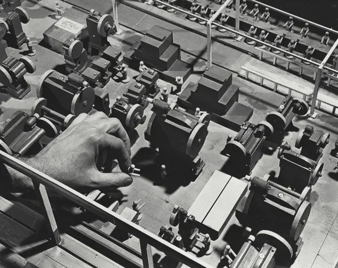 Vintage photograph. Into a section of a plant model of the Ford Motor Company a plastic model figure incorporating the dimensions of the average sized man is being placed in correct position on floor near model of giant hydraulic press.