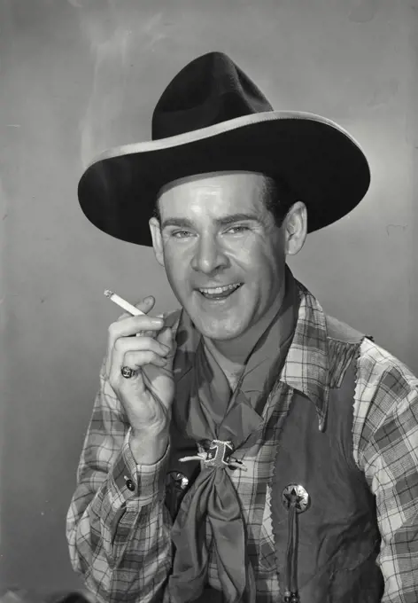 Vintage photograph. Dark haired man wearing western outfit and cowboy hat holding lit cigarette in hand