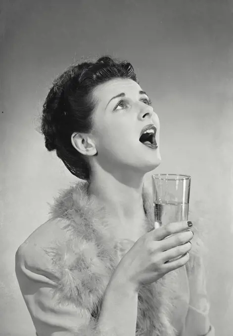 Vintage photograph. Woman holding glass with mouth open looking above