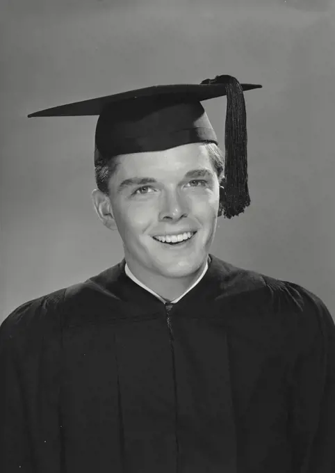 Vintage photograph. Smiling young man wearing graduation gown and cap