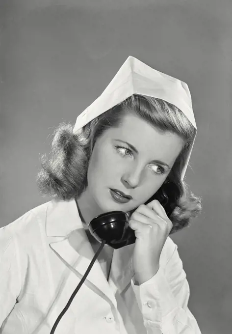 Vintage photograph. Smiling young blonde woman wearing white nurse uniform and cap talking on phone looking right