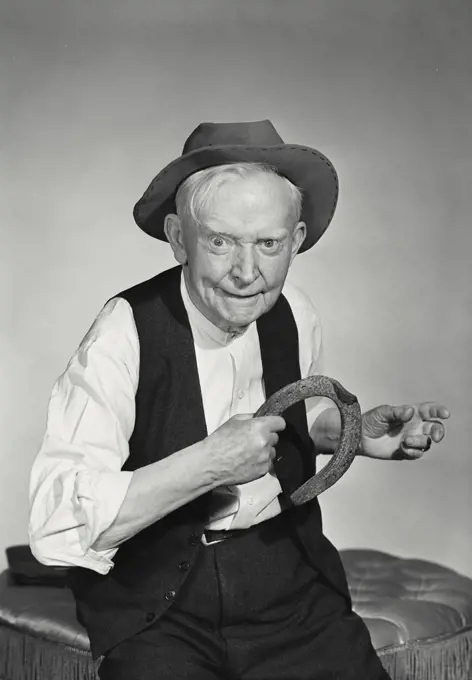 Prankster old man wearing hat and vest about to throw horseshoe
