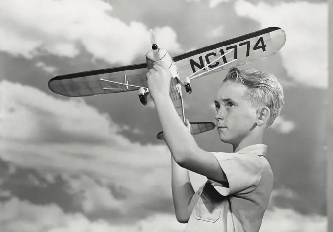 Boy spinning propeller on toy airplane in front of cloud sky background