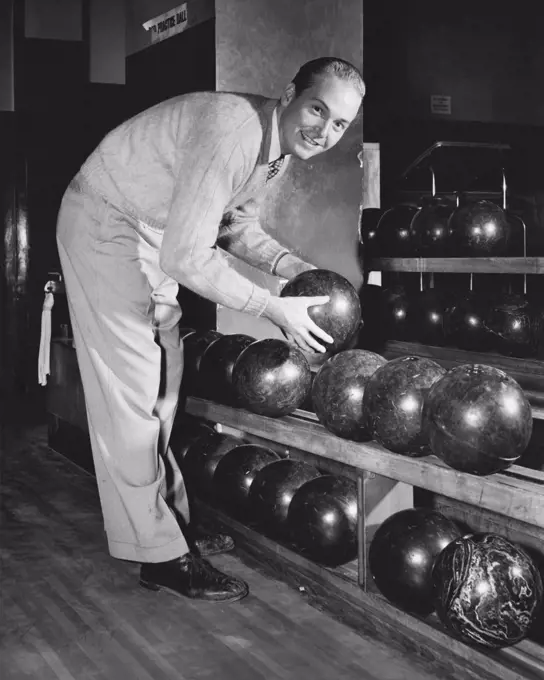 Vintage Photograph. Young adult man reaching for bowling ball on shelf