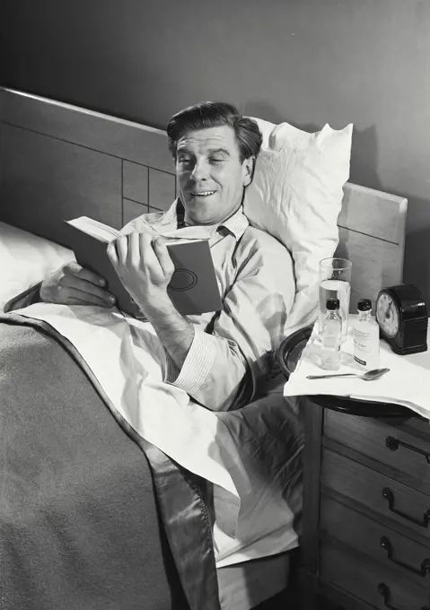 Vintage Photograph. Buck McHugh. Model Released. Sick man in pajamas sitting up and reading book. Frame 1