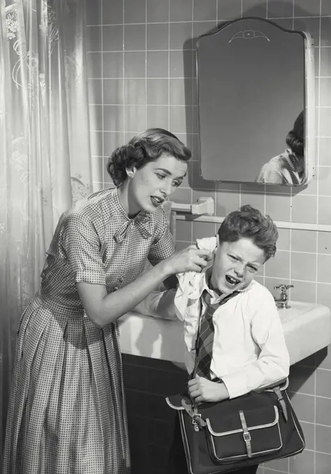 Vintage photograph. Mother cleaning unhappy young boys ear.