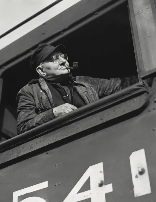 Vintage photograph. Engineer looking out of cab of a diesel locomotive with pipe in mouth