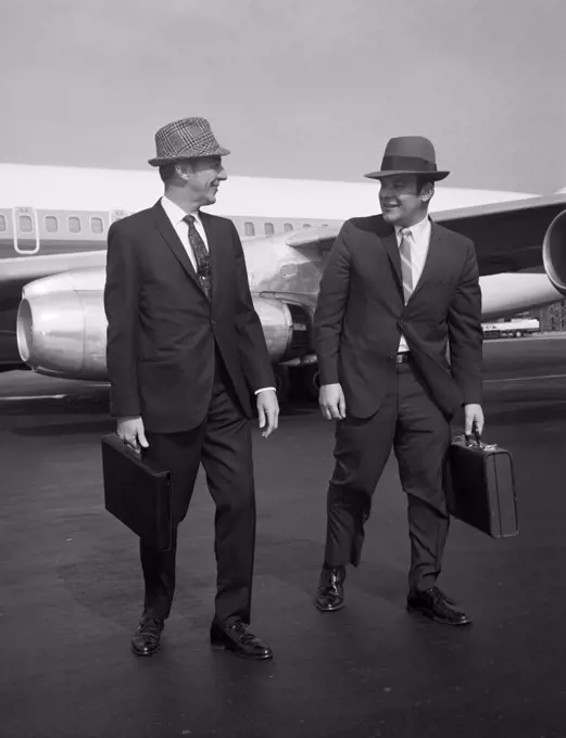 Two men walking along airplane at airport