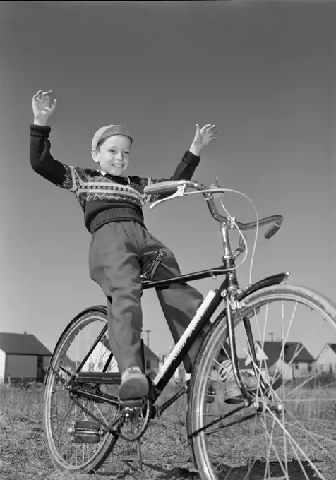 Boy riding bicycle with arms raised