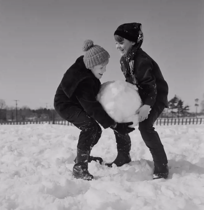 Two kids carrying large snowball