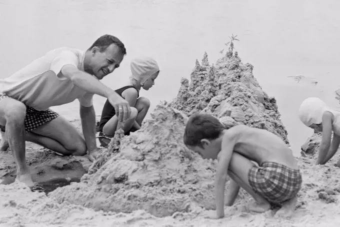 Father with three children building sand castle on beach