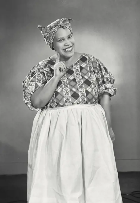 African American woman wearing head scarf and apron holding up index finger smiling