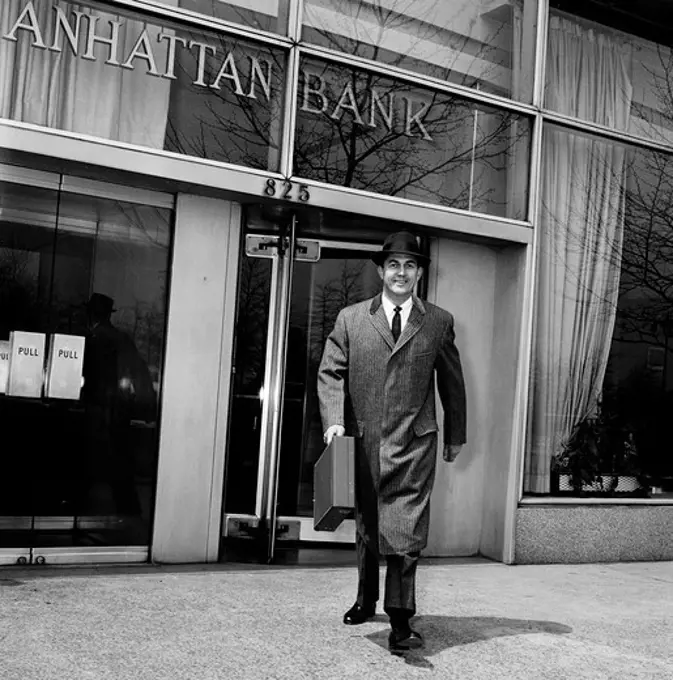 Businessman walking out of bank carrying briefcase