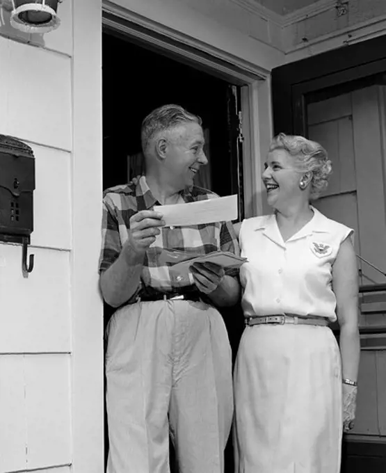 Smiling senior couple standing at front door, holding letters