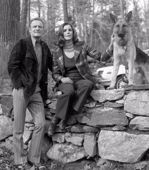 Portrait of mature couple with dog sitting on stone wall